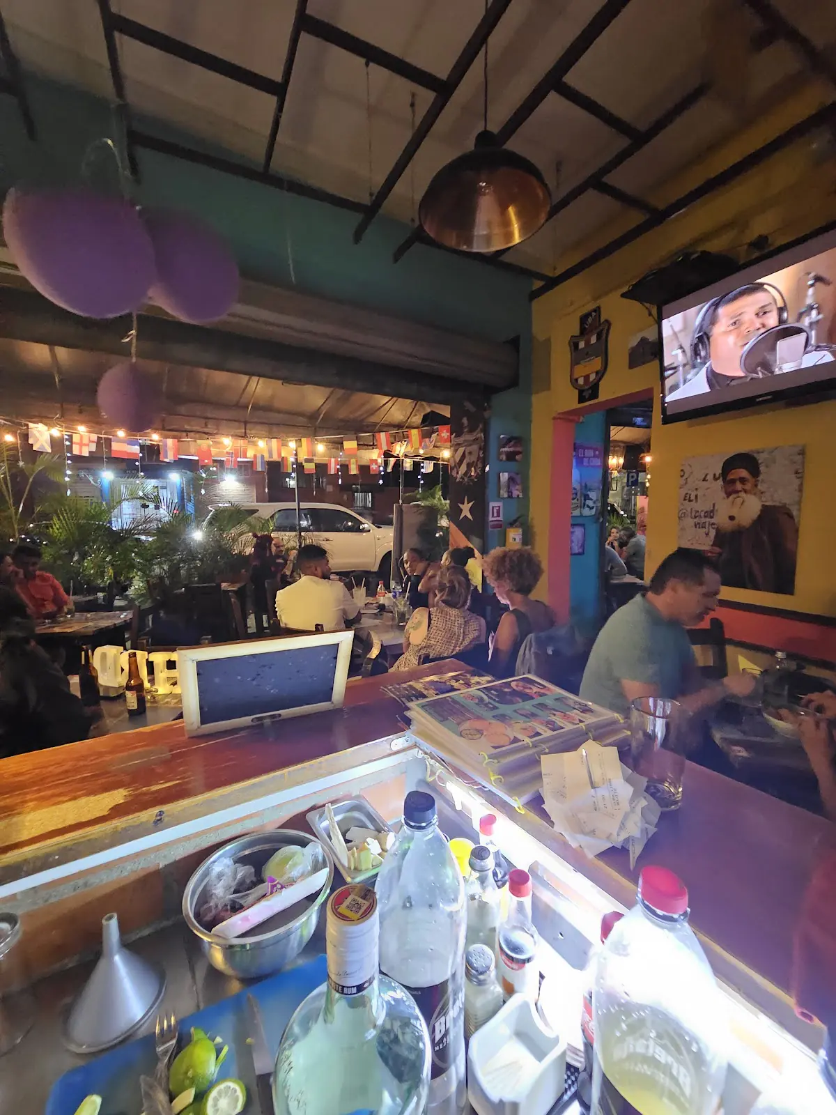La barra y el salón de La Bodeguita Havanera de noche, con luces y banderas