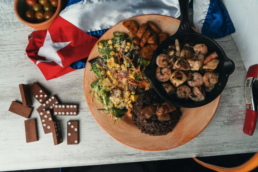 Camarones Cienfuegos con arroz, maduro y ensalada junto a una bandera cubana y fichas de dominó